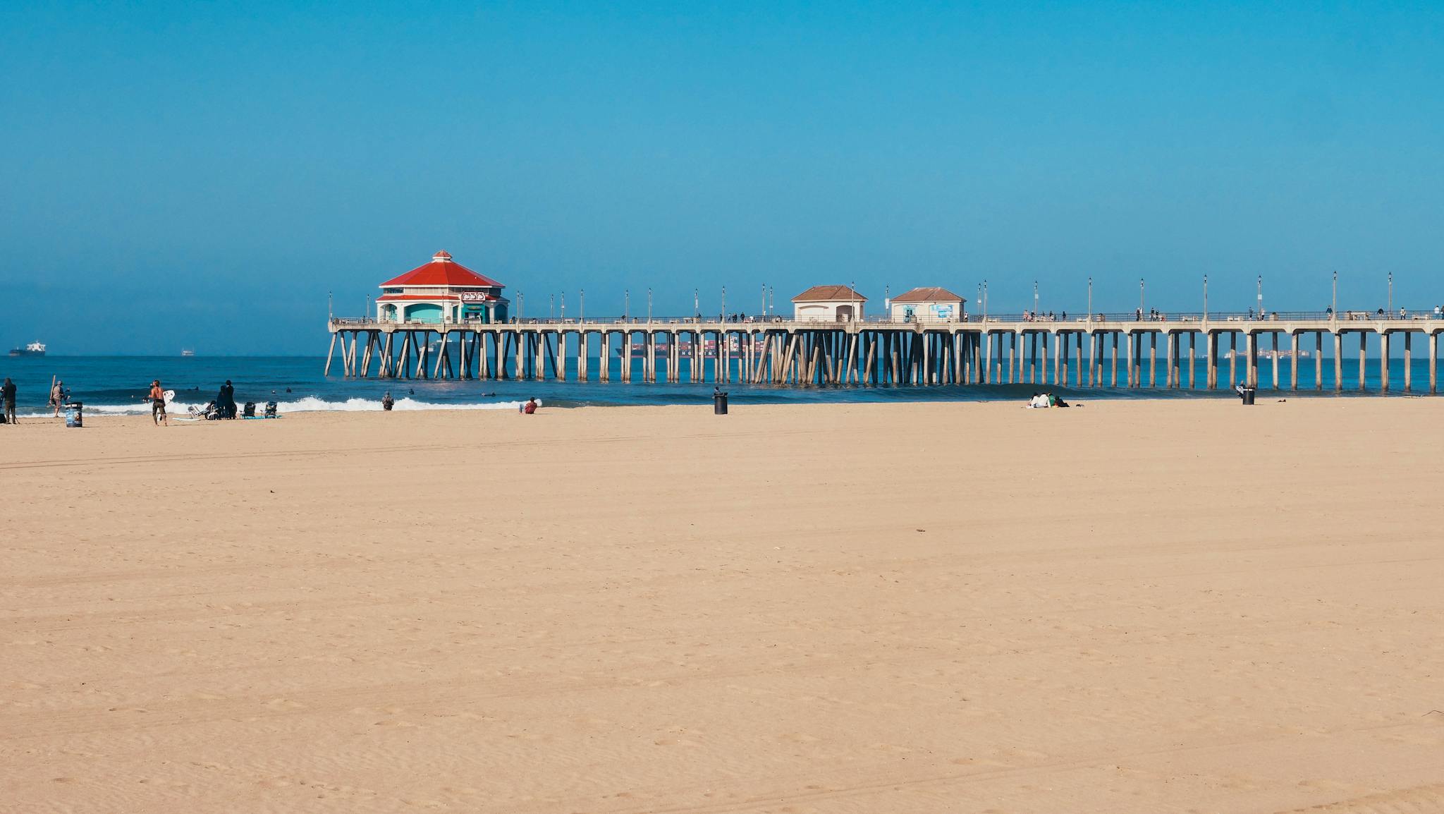 Sunny day at the beach with a distant pier and open blue sky, perfect for summer relaxation.