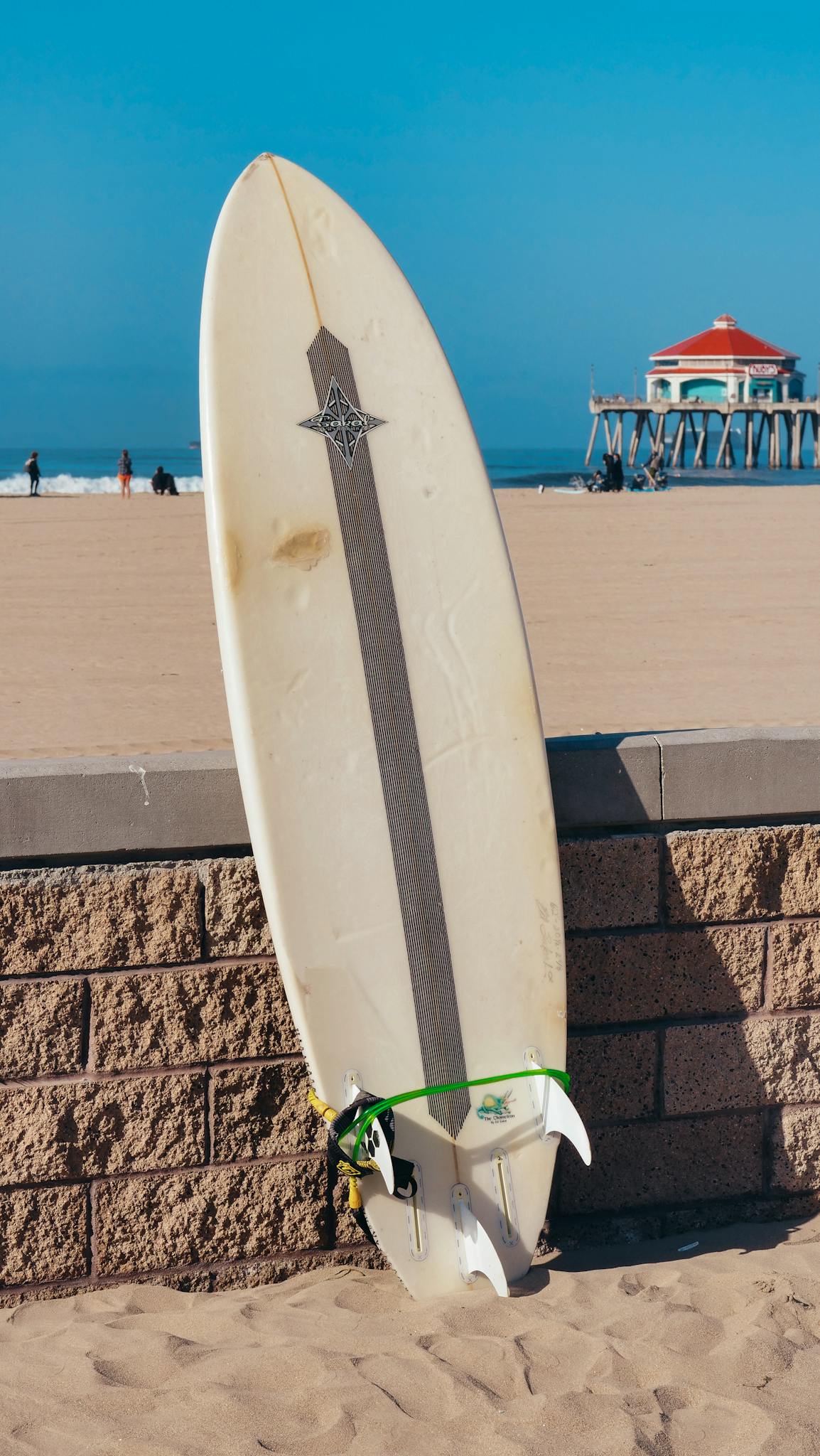 Surfboard against a sandy beach and pier backdrop, perfect for summer and surf lifestyle themes.