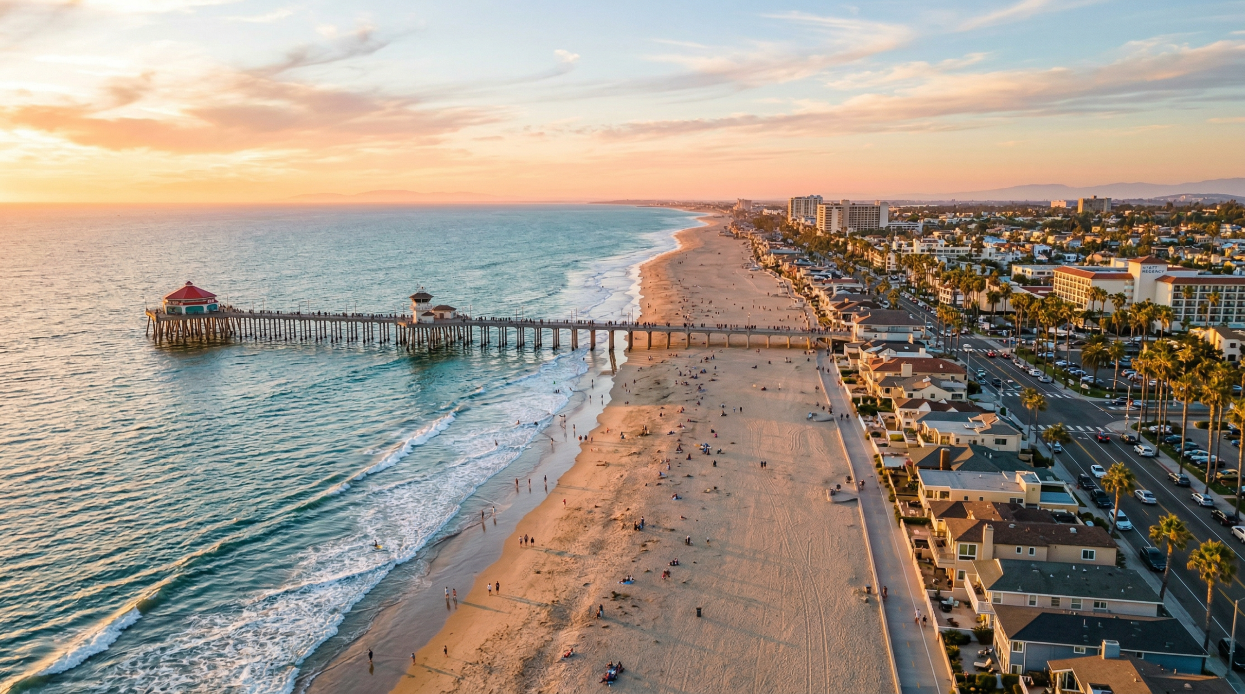 Aerial view of Huntington Beach neighborhoods along the coastline at golden hour — the iconic pier, wide sandy beach, and coastal homes along PCH